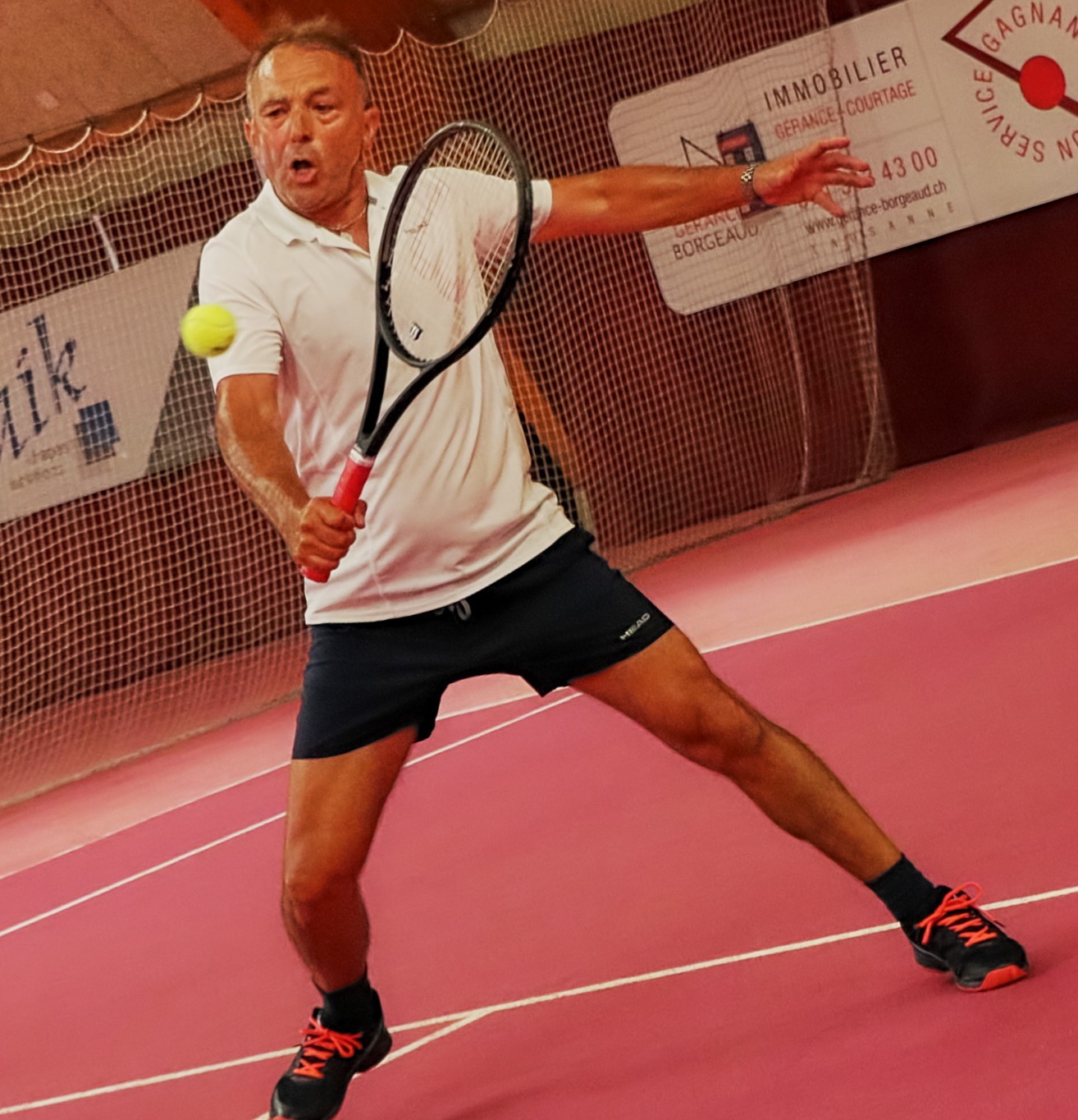 Pascual Alcaraz, tennis coach, hitting a backhand on an indoor court